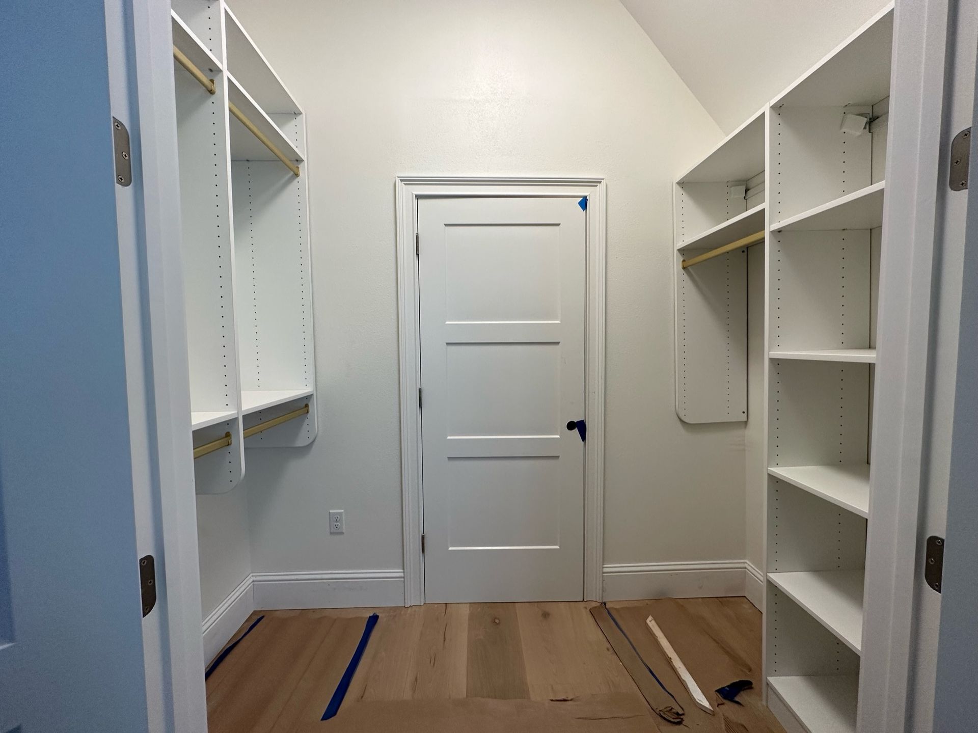 Empty white walk-in closet with shelves and door; light wood floor; white walls.