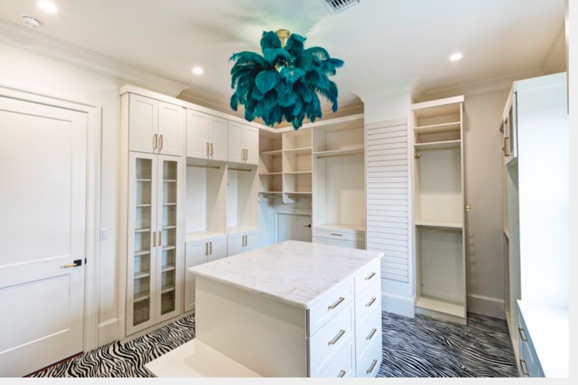 Elegant white closet with central island and teal feathered chandelier. Zebra print floor.