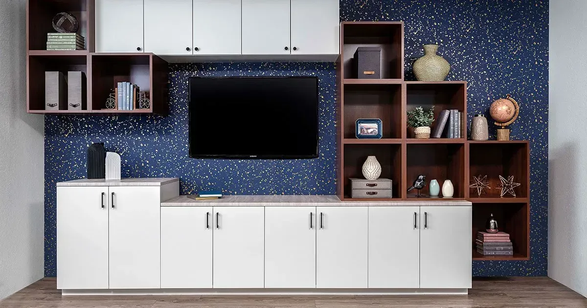 Built-in home entertainment center with white and brown cabinets, a TV, and decorative shelves against a blue wall.
