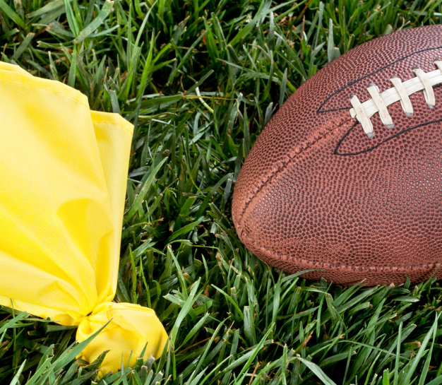 Football and yellow penalty flag on green grass