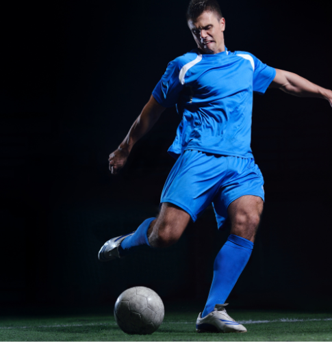 Soccer player in blue uniform kicking a ball on a dark field