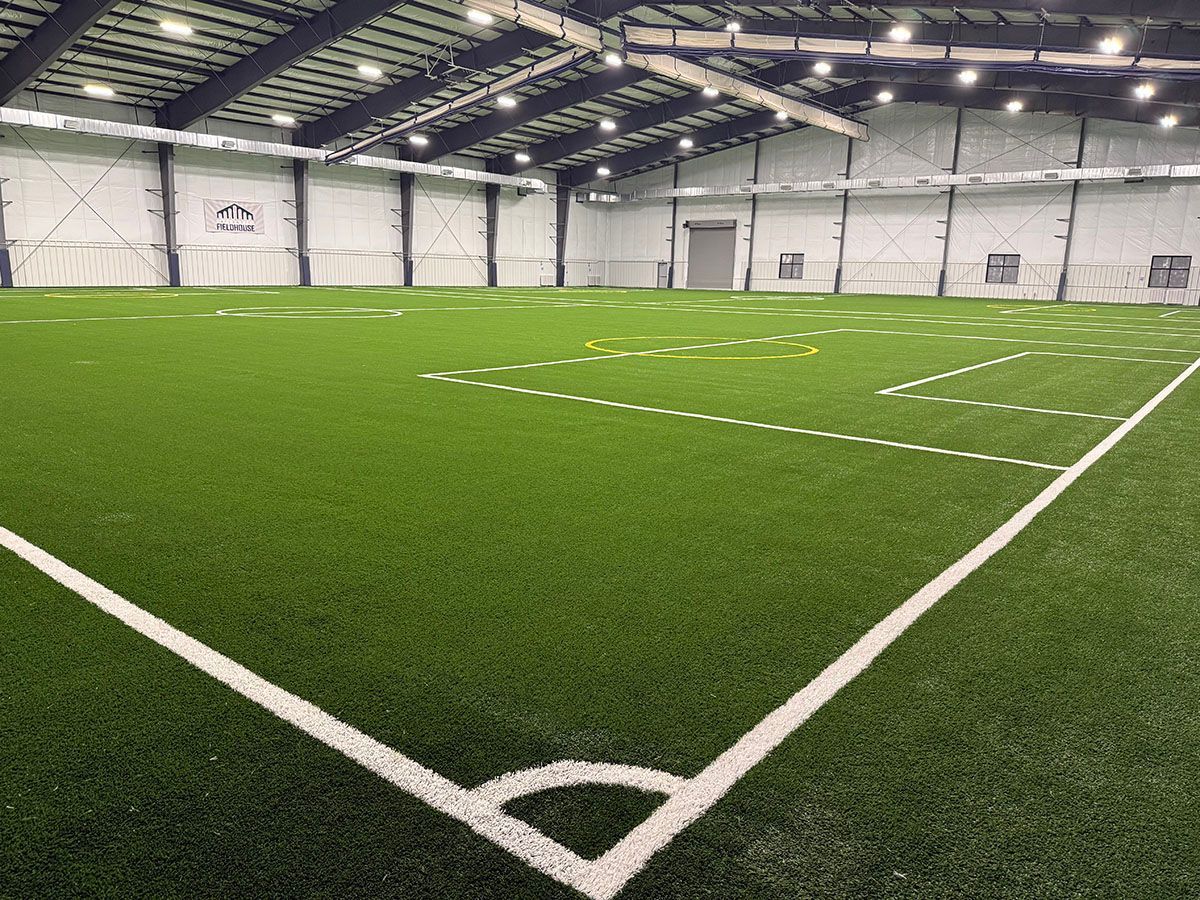 Indoor soccer field with green turf, white boundary lines, and netted walls under bright lights