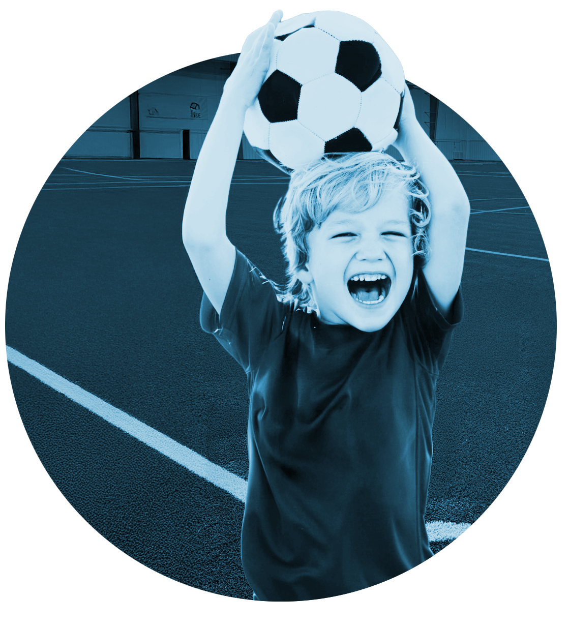 Child holding a soccer ball overhead on a field, smiling and shouting in a blue-tinted photo.
