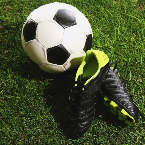 Soccer ball and black cleats with neon green accents on grass