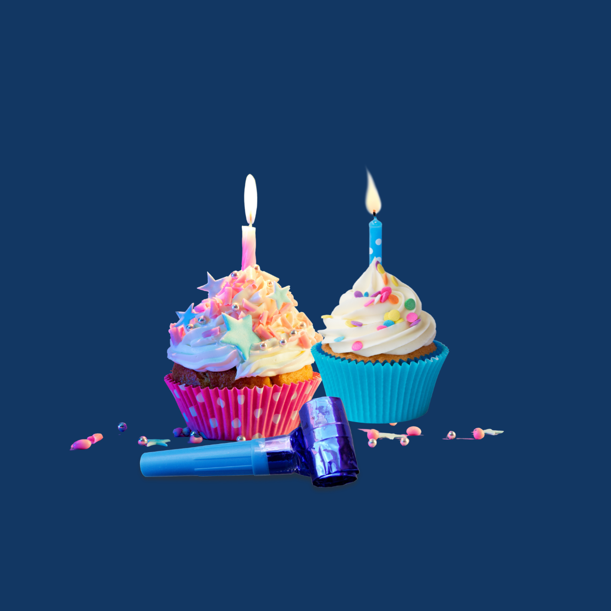 Two lit cupcakes with colorful frosting and a blue party blower on a dark blue background