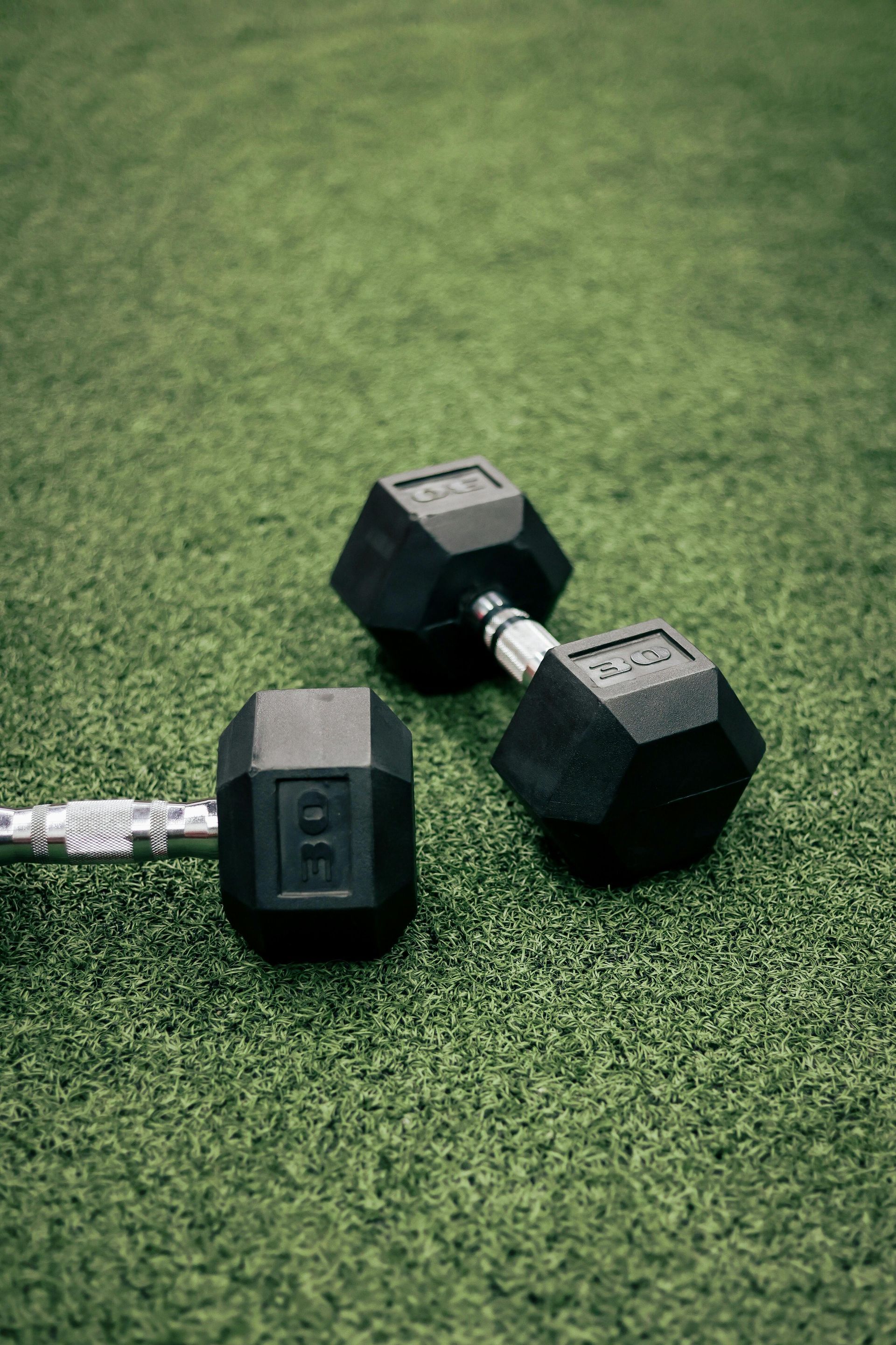 Two black hex dumbbells on green turf, one with a visible weight label
