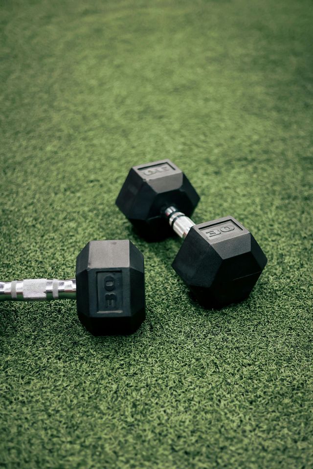 Two black hex dumbbells on green turf, one with a visible weight label