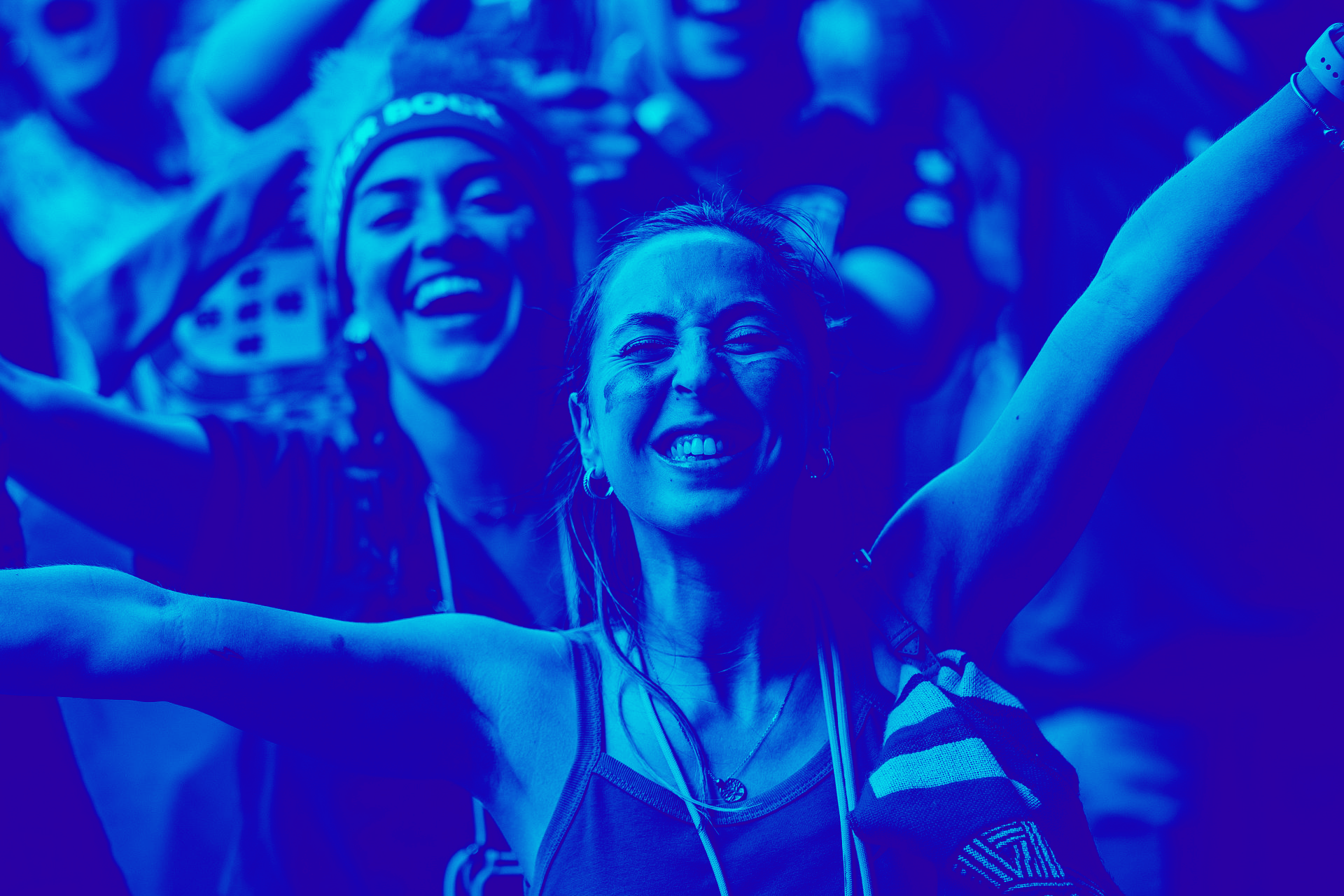 Two smiling concertgoers with arms raised, bathed in blue stage lighting