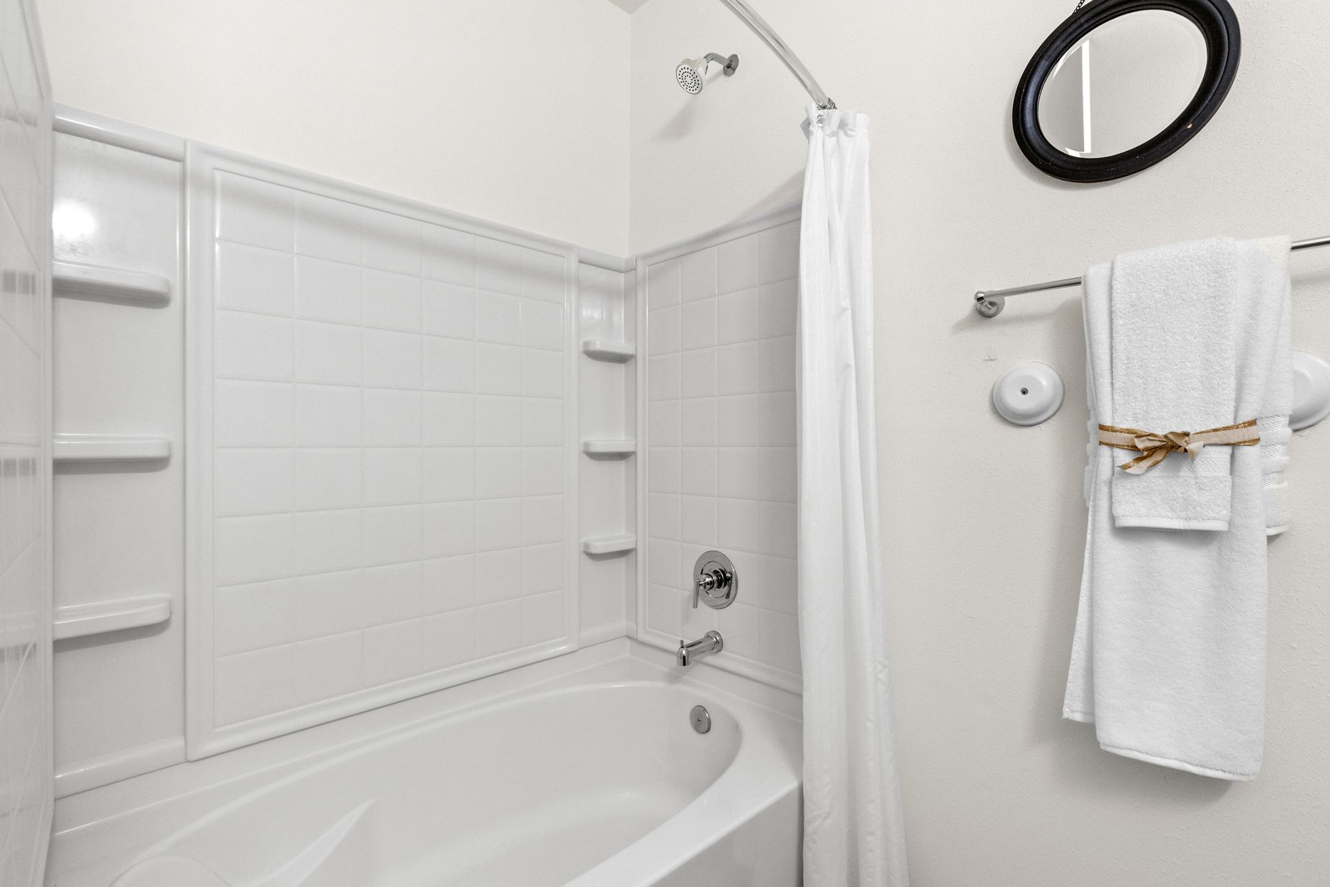White bathroom with bathtub, tiled shower surround, towel rack, and round mirror