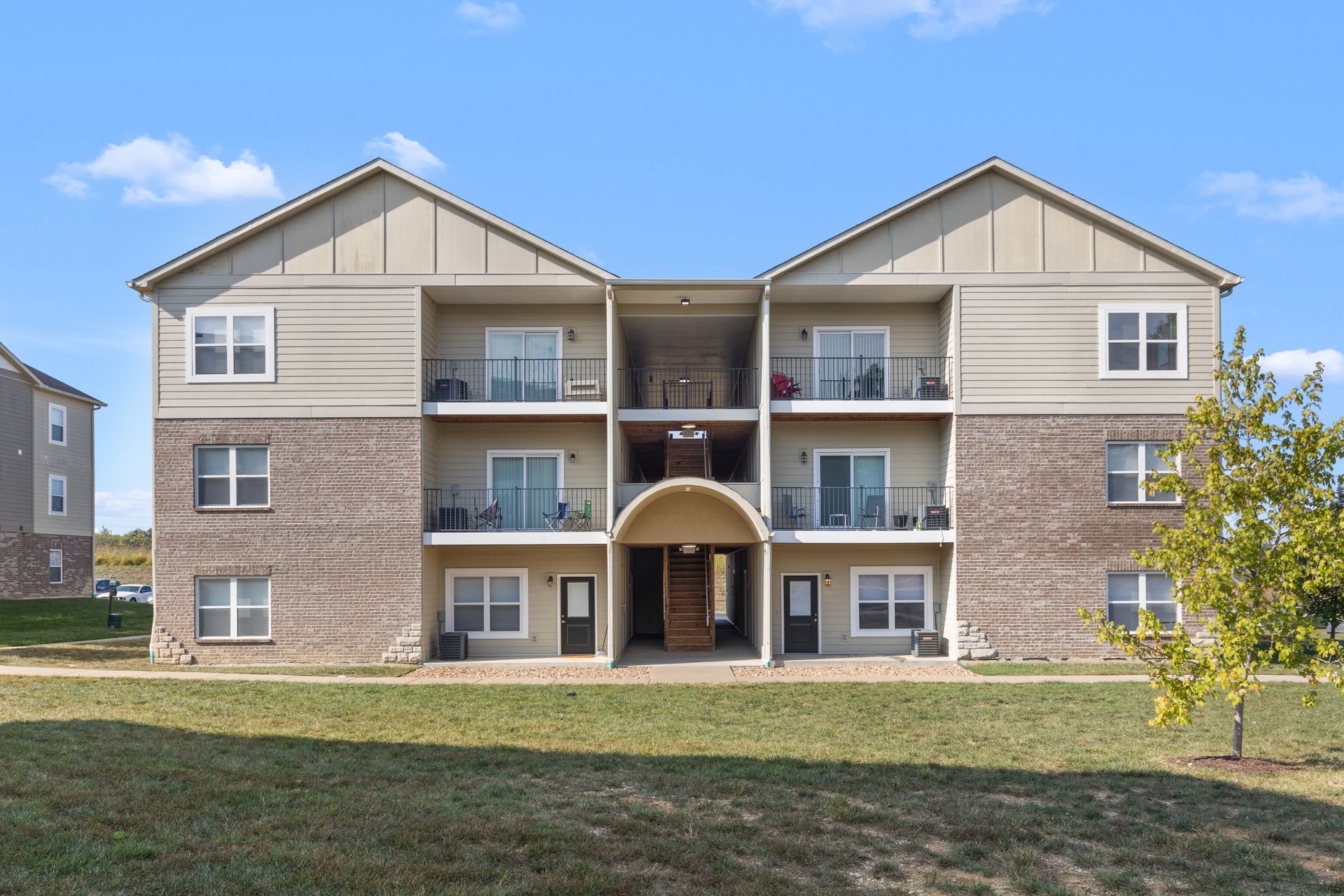 Three-story apartment building with balconies and a central entrance under a clear blue sky