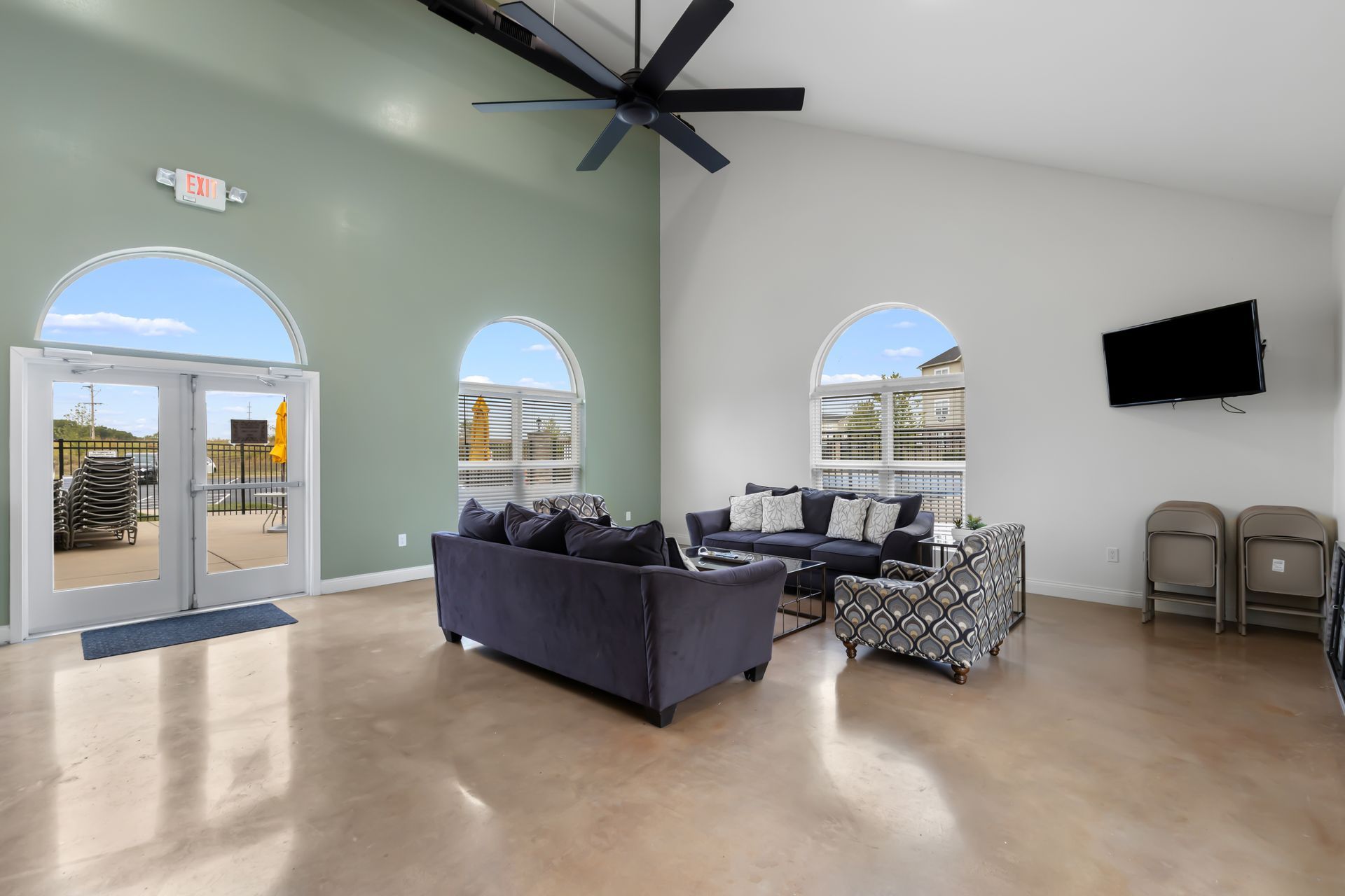 Bright living room with high ceiling, blue and patterned sofas, wall-mounted TV, and arched windows.