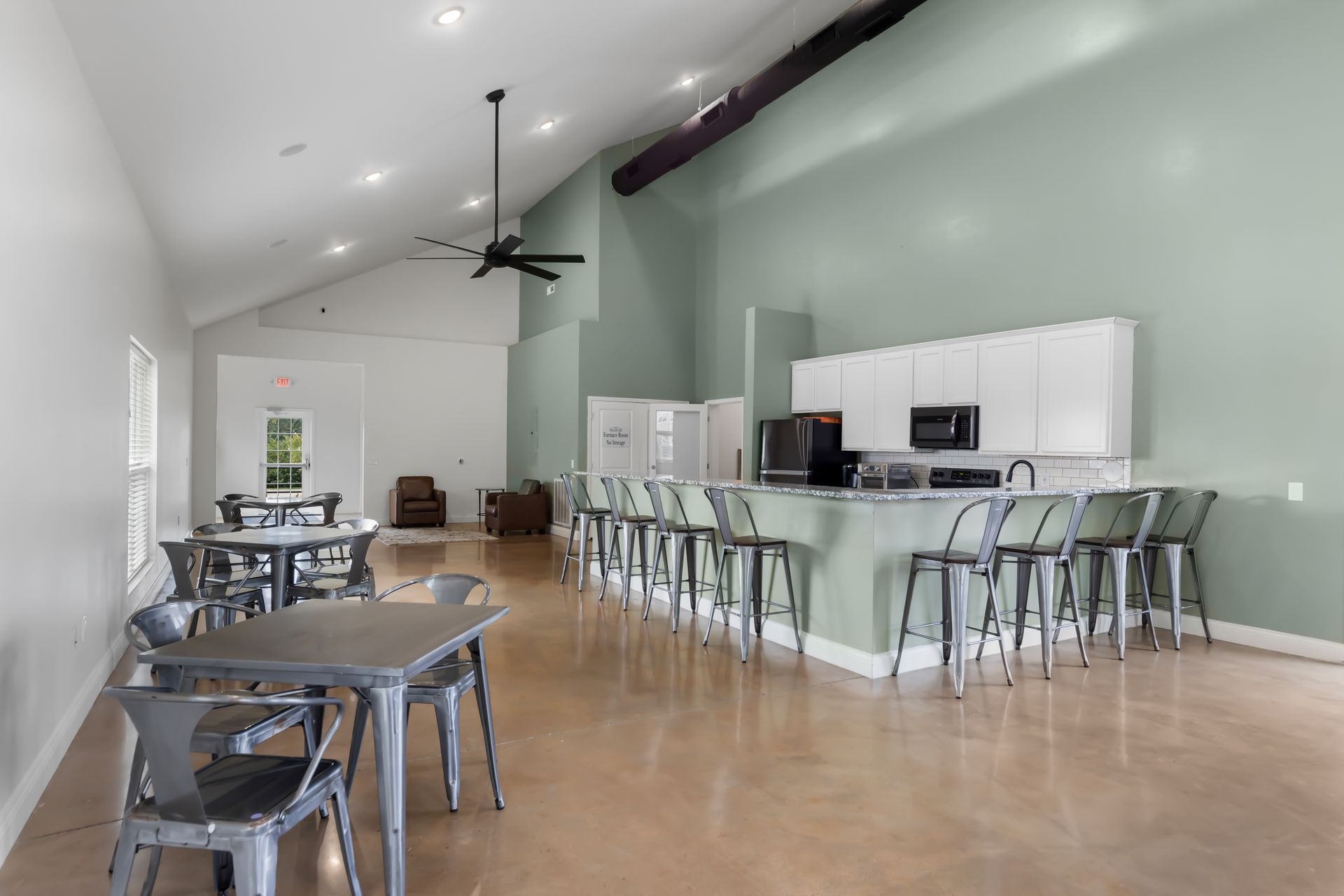 Bright open cafe with mint-green walls, white tables, and a long counter with stools and ceiling fans