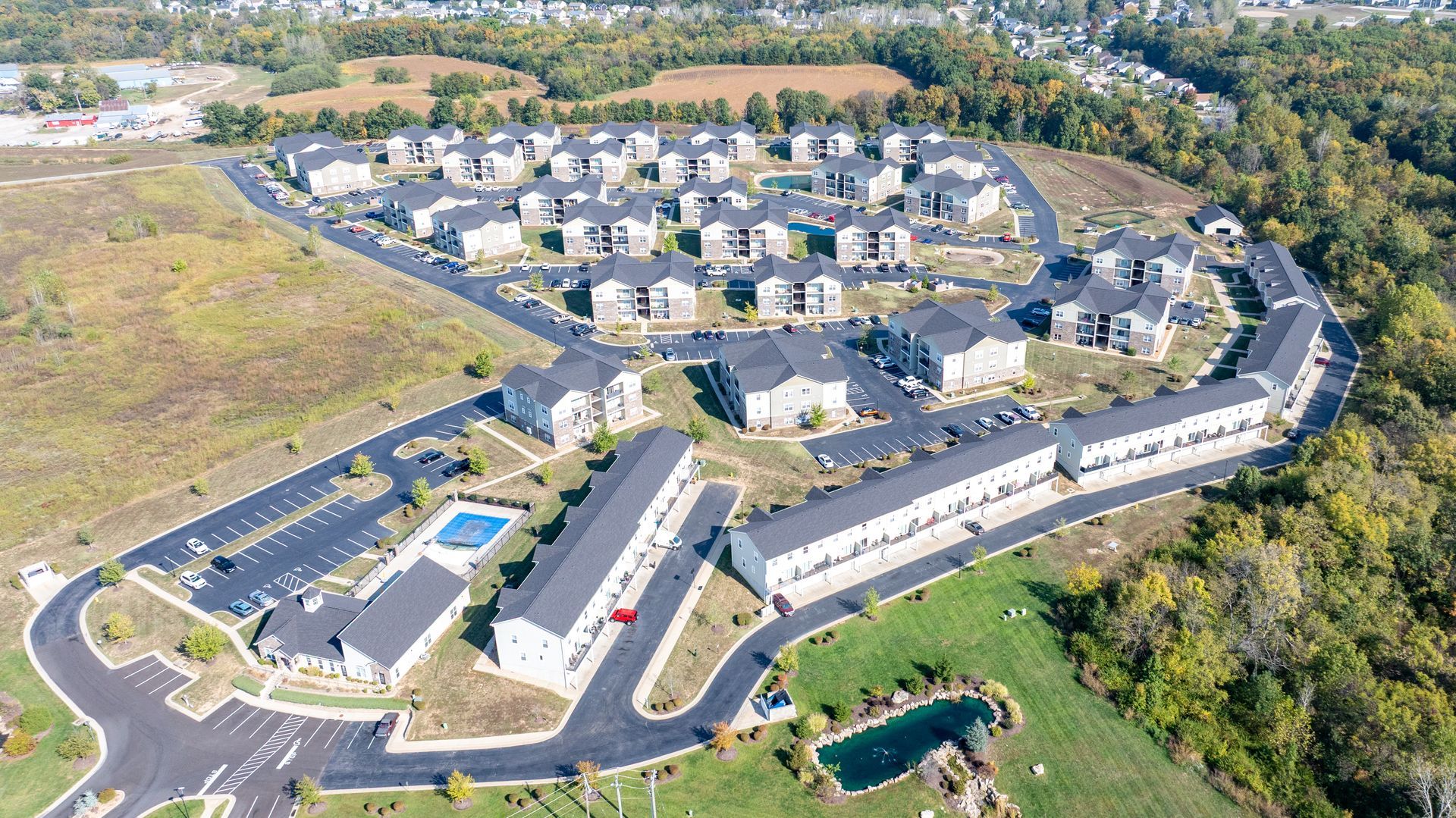 Aerial view of a residential apartment complex with parking lots, roads, and surrounding green space.