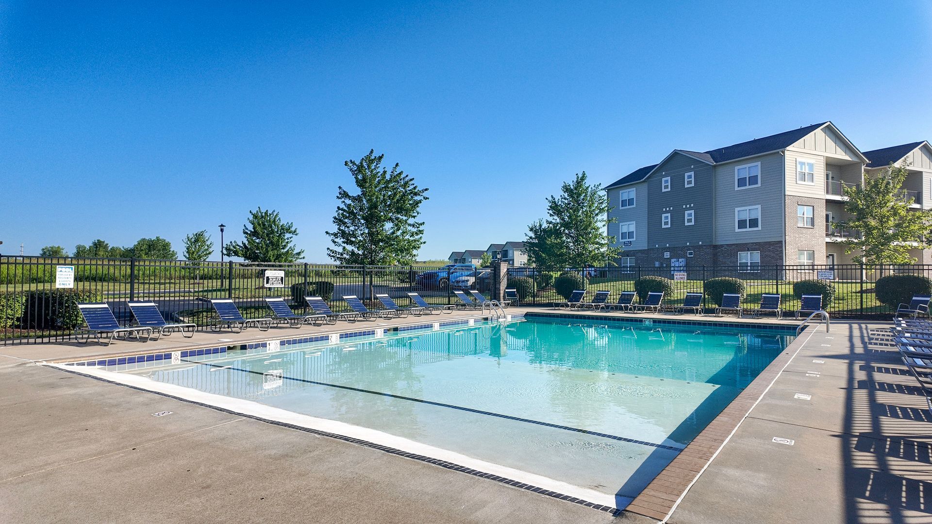 Outdoor apartment pool with clear blue water, lounge chairs, and a sunny courtyard setting