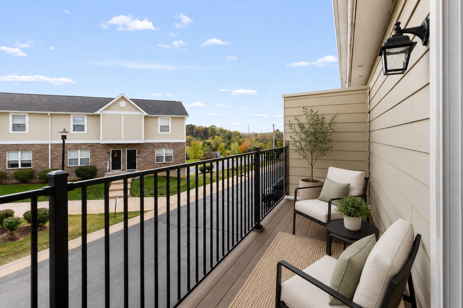 Apartment balcony with black railing, seating, and a view of townhouses and blue sky