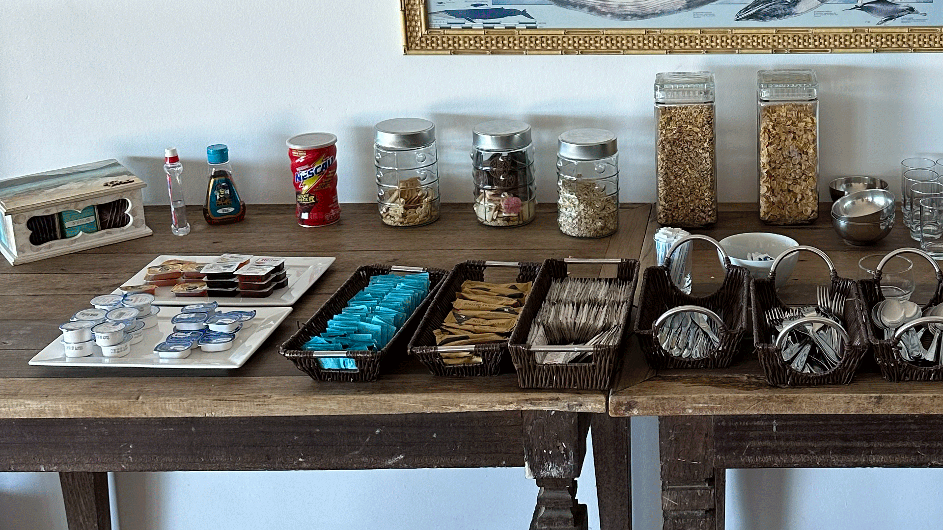 Uma mesa de madeira exibe potes, recipientes de comida e pratos em uma sala iluminada.
