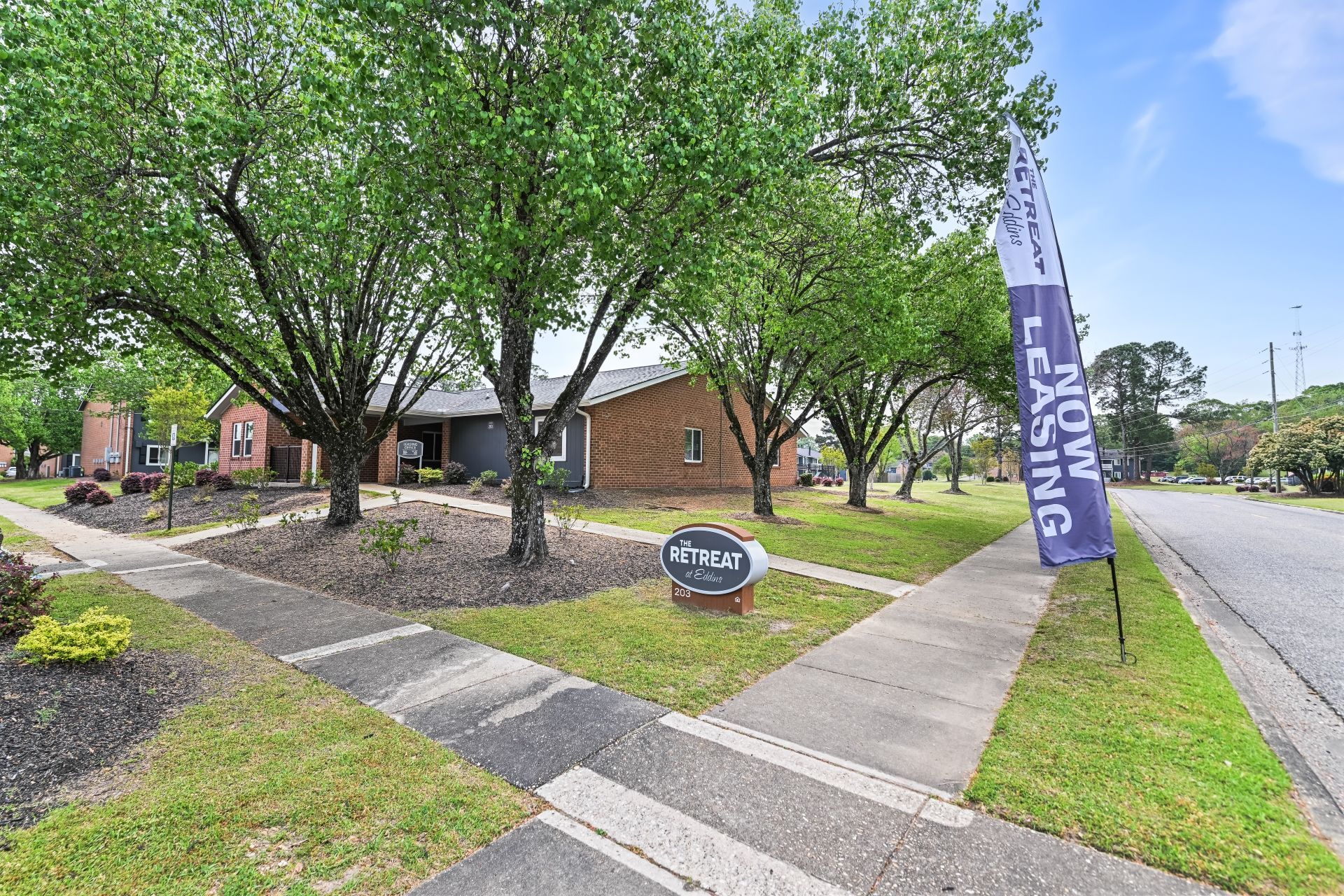 A brick apartment building with trees, a sidewalk, and a blue 