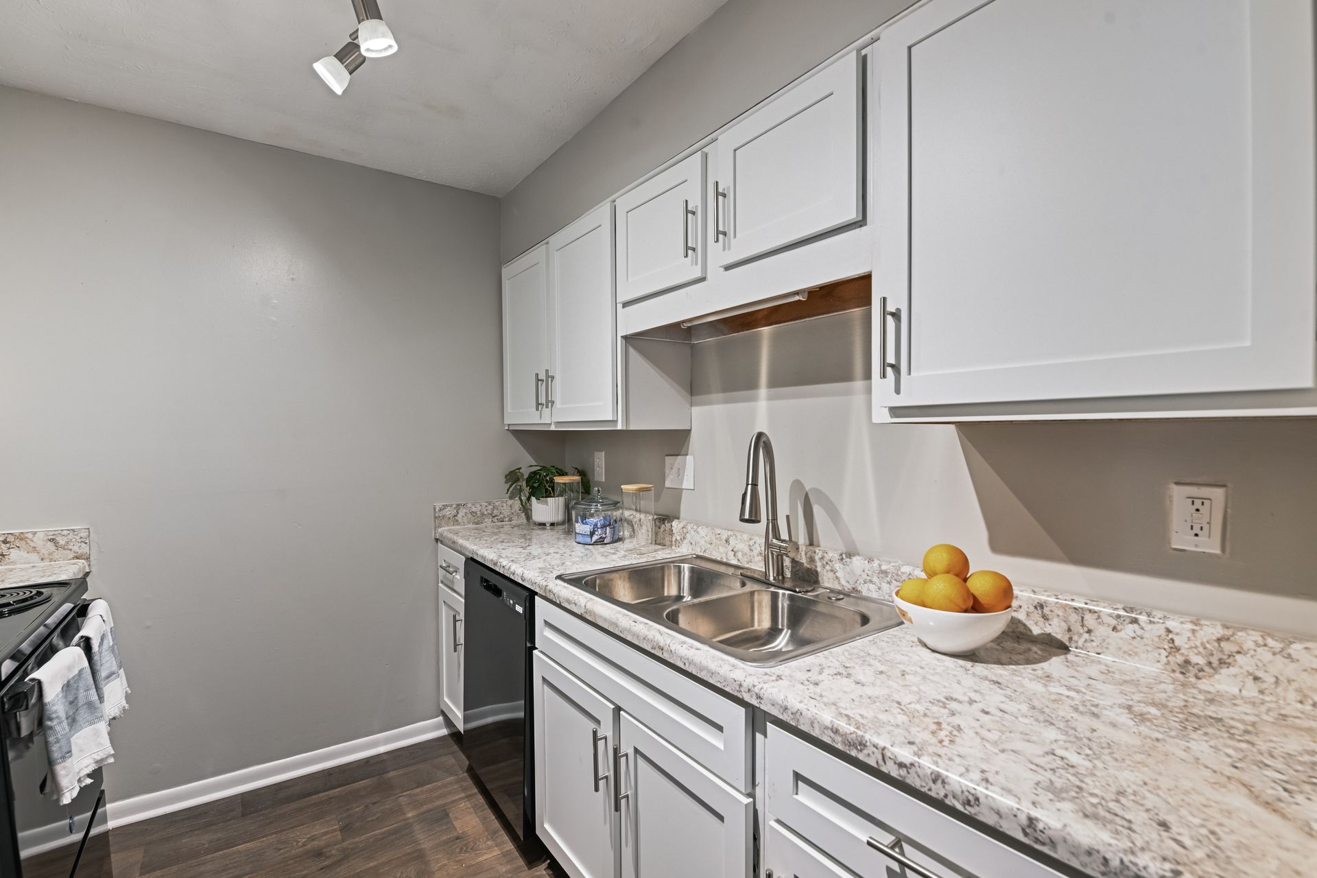 A bright kitchen with white cabinets, light countertops, a stainless steel sink, and gray walls.