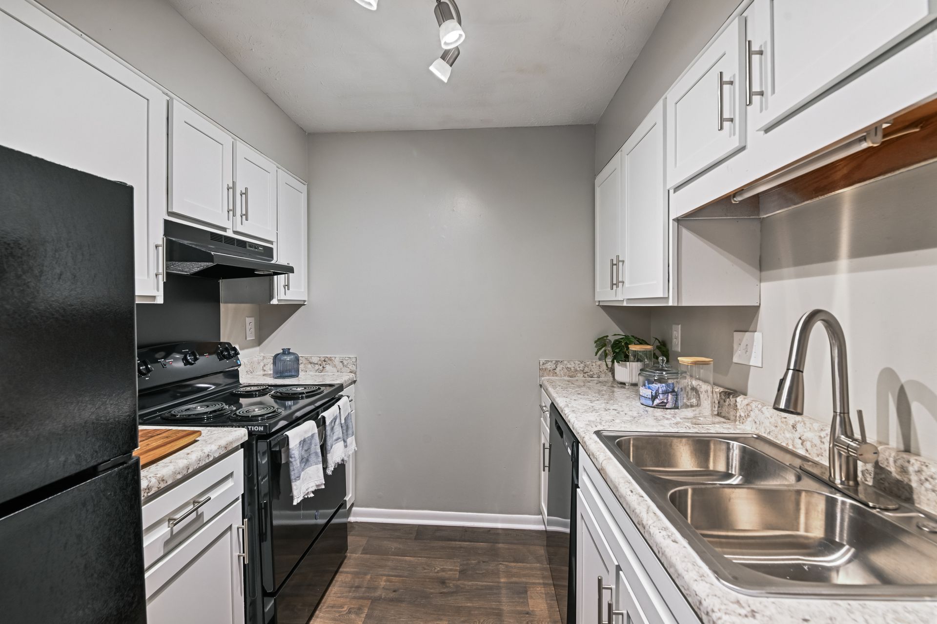 A galley-style kitchen with white cabinets, light countertops, black appliances, and a stainless steel sink.