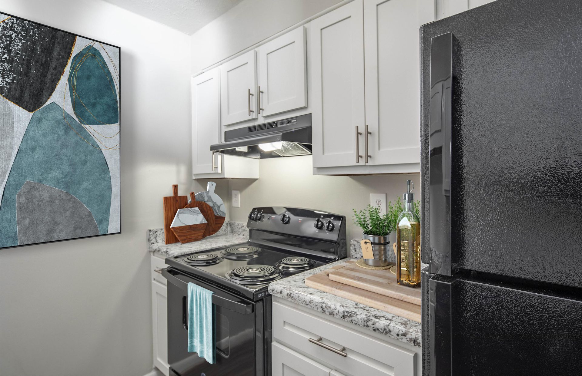 A modern kitchen featuring white cabinets, grey granite countertops, a black stove and refrigerator, and abstract wall art.