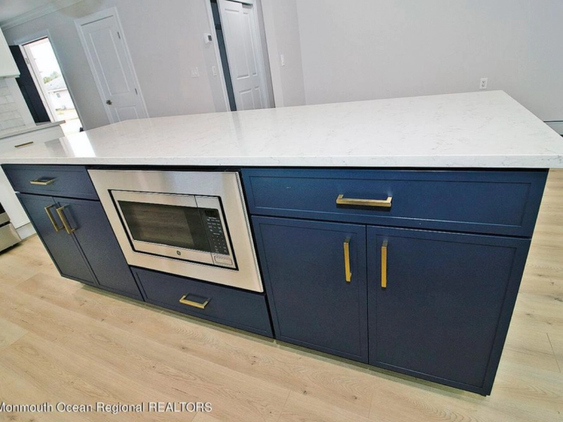 Blue kitchen island with a white countertop, a built-in microwave, and gold hardware. Located in a kitchen with light wood flooring.