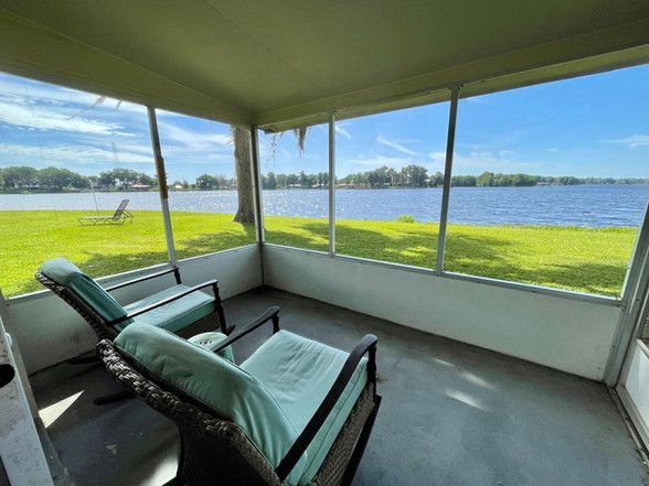 A screened in porch with chairs and a view of a lake.