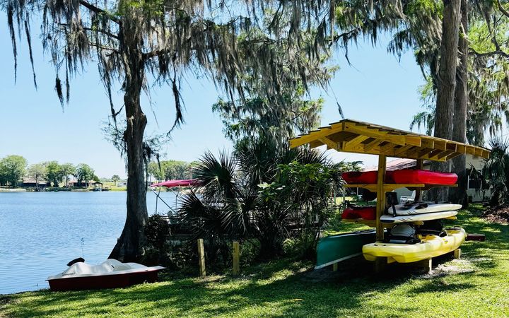 A row of kayaks are sitting on the grass next to a lake.