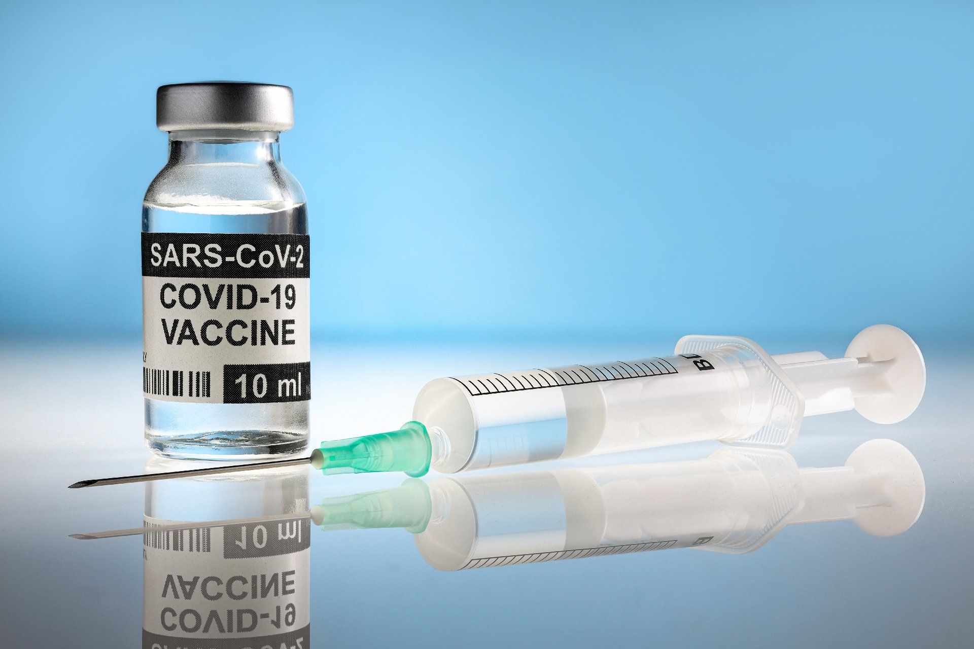 SARS-CoV-2 COVID-19 vaccine vial beside a syringe on a blue background