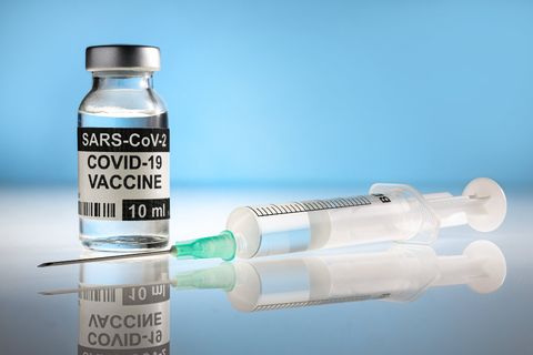 COVID-19 vaccine vial and syringe on a blue surface with reflection