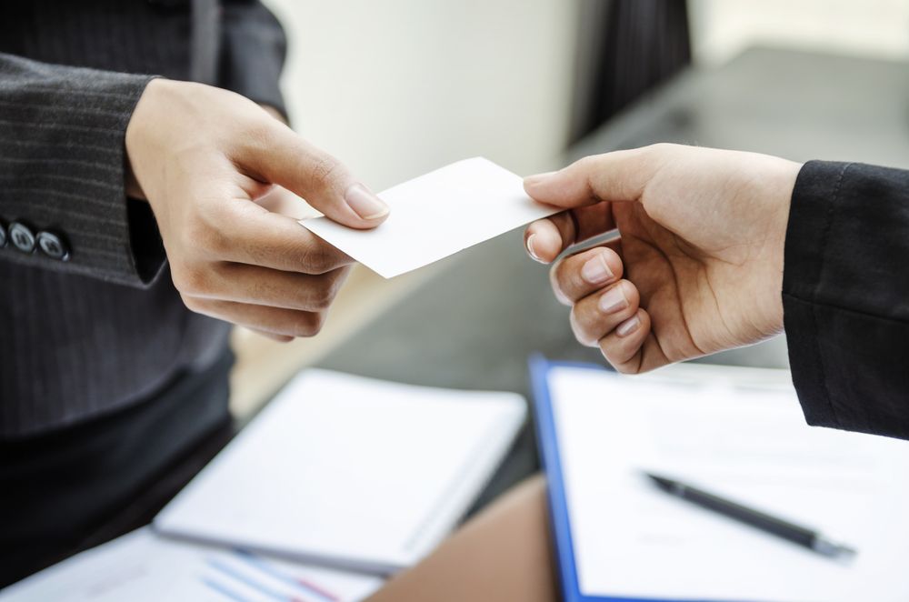 Two People Exchanging a White Card Across a Desk in a Business Setting — Lehmann Print Solutions in Bowen, QLD