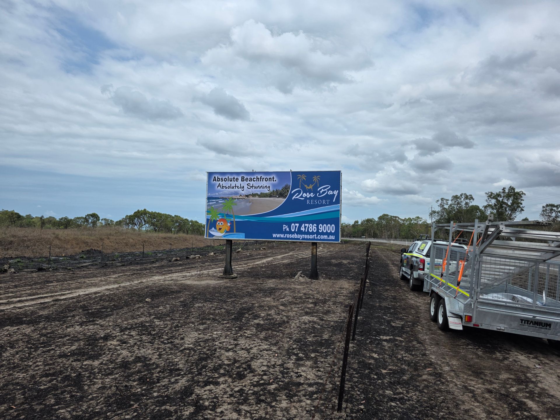 Blue Roadside Sign Beside a Dirt Road Under Cloudy Sky — Lehmann Print Solutions in Bowen, QLD