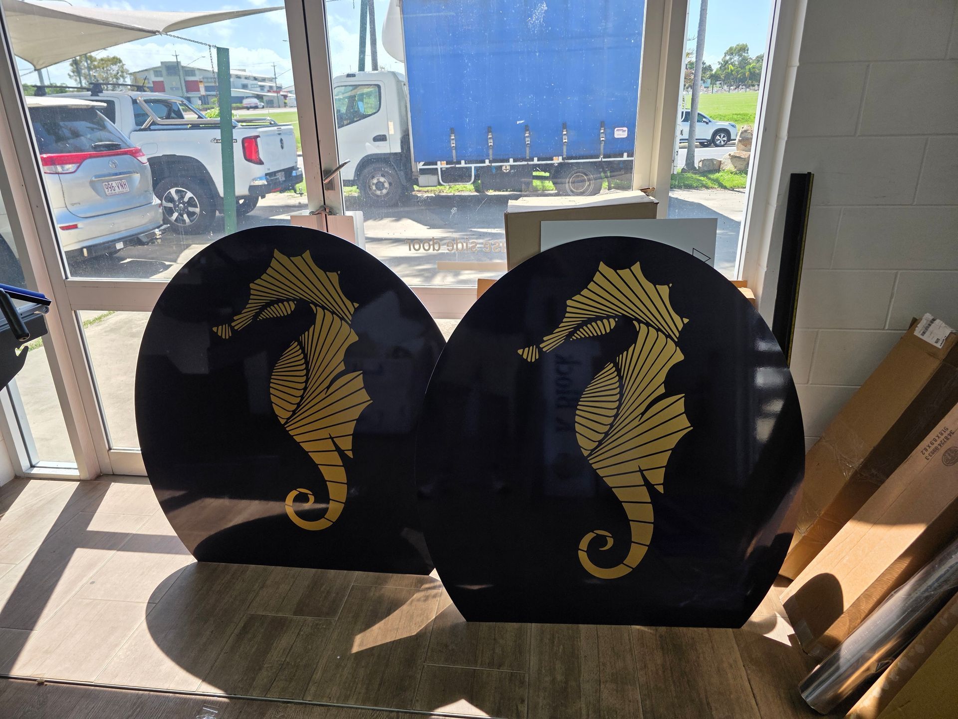 Two black seahorse-shaped plaques with gold designs displayed in front of a store window. — Lehmann Print Solutions in Bowen, QLD