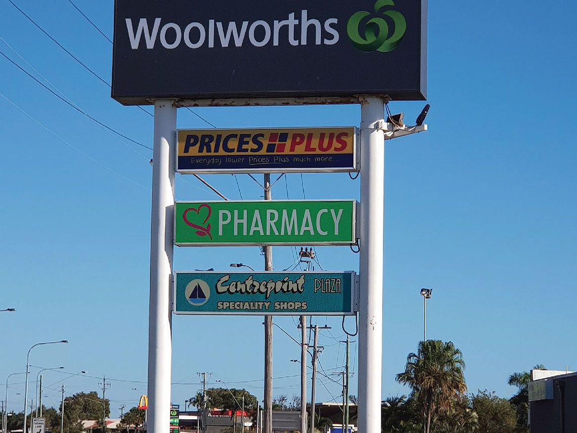Woolworths Storefront Signs Over a Roadside Scene Under a Clear Blue Sky — Lehmann Print Solutions in Bowen, QLD