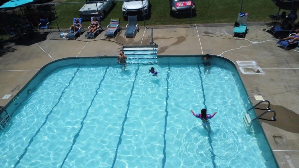 Outdoor swimming pool with several people swimming and lounging nearby on a sunny day