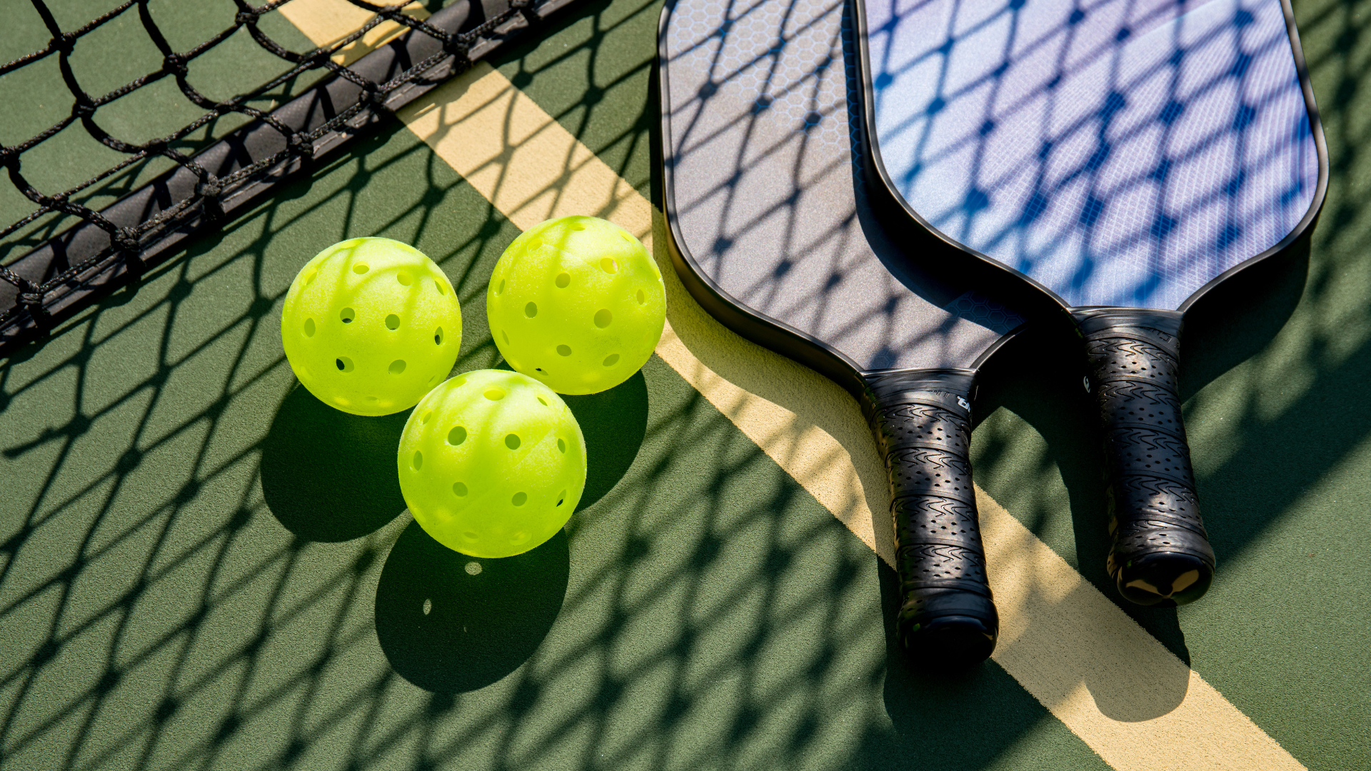 Two tennis paddles beside three neon yellow tennis balls on a court net