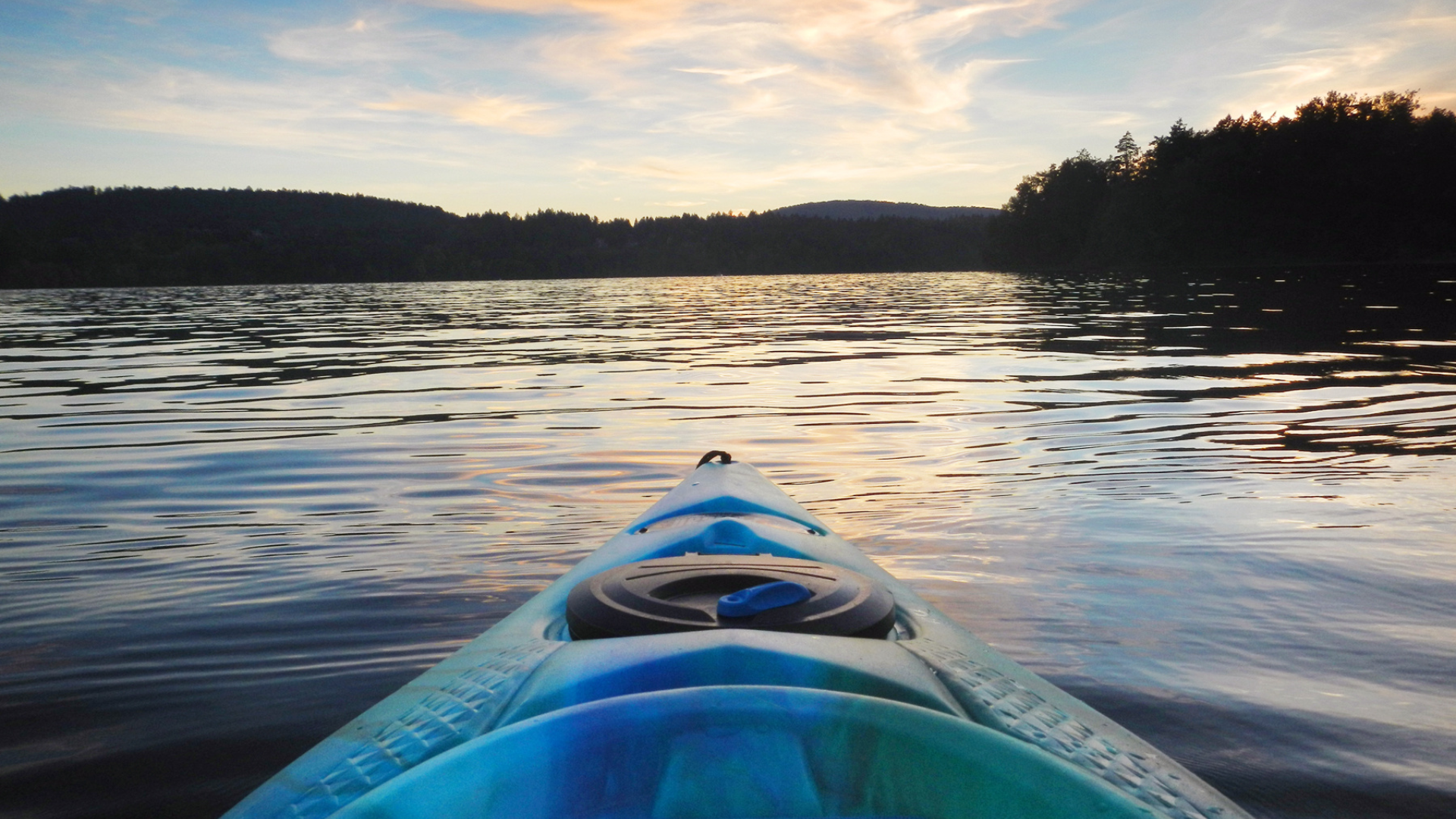 Blue kayak on calm lake at sunset, facing distant tree-lined shore.