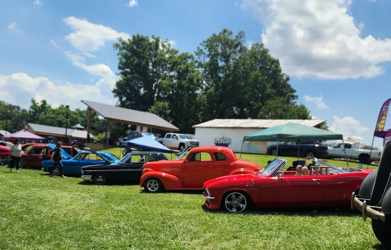 Classic cars displayed on a sunny grassy field at an outdoor car show under tents and umbrellas