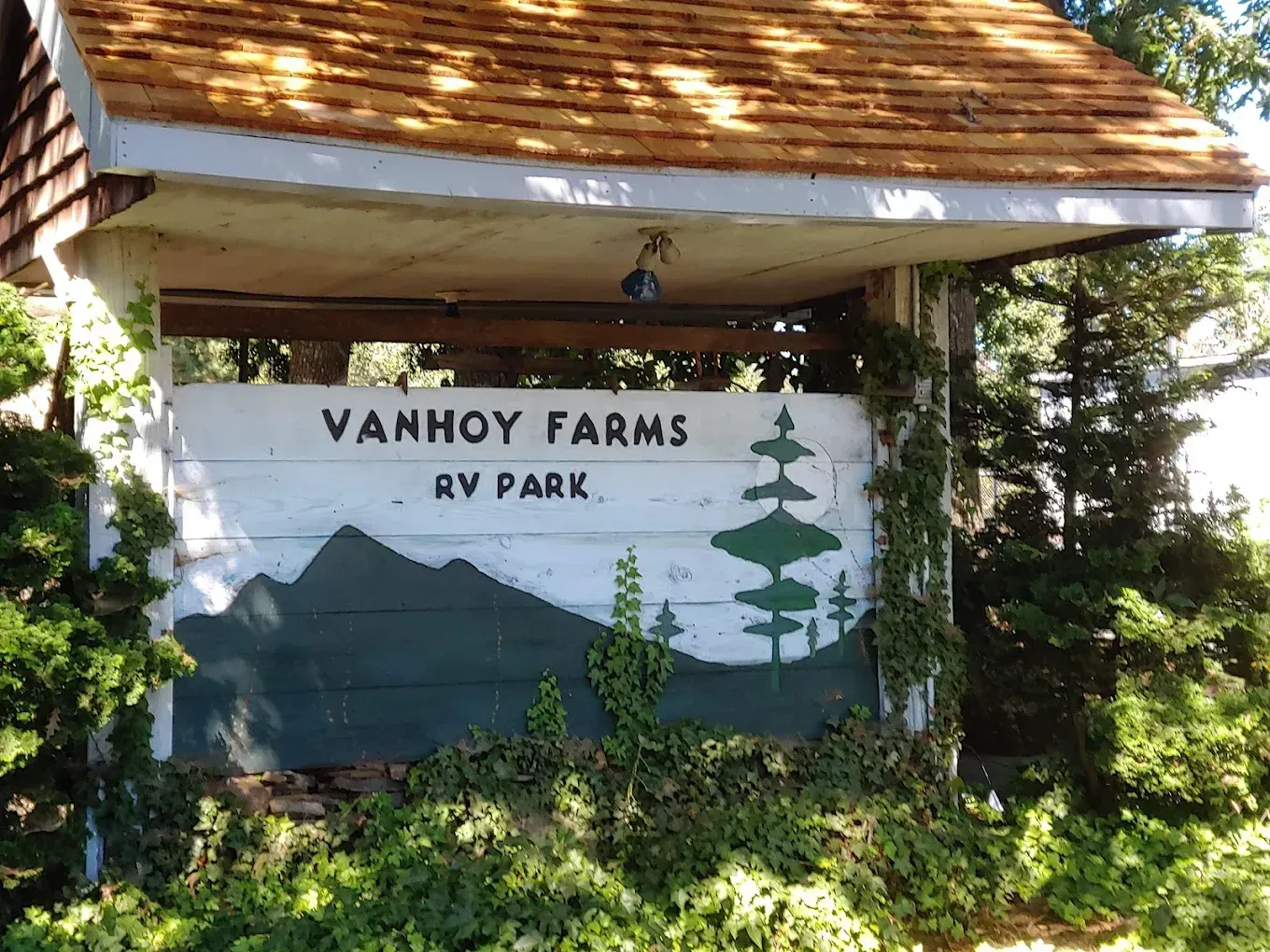 Van Hoy Farms RV Park sign under a rustic roof, painted with mountains and trees