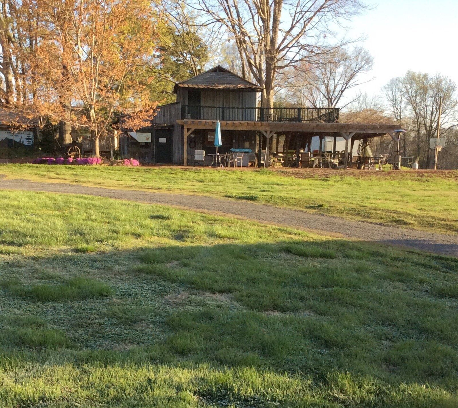 Rustic house with porch in a grassy park, framed by autumn trees and warm sunlight.