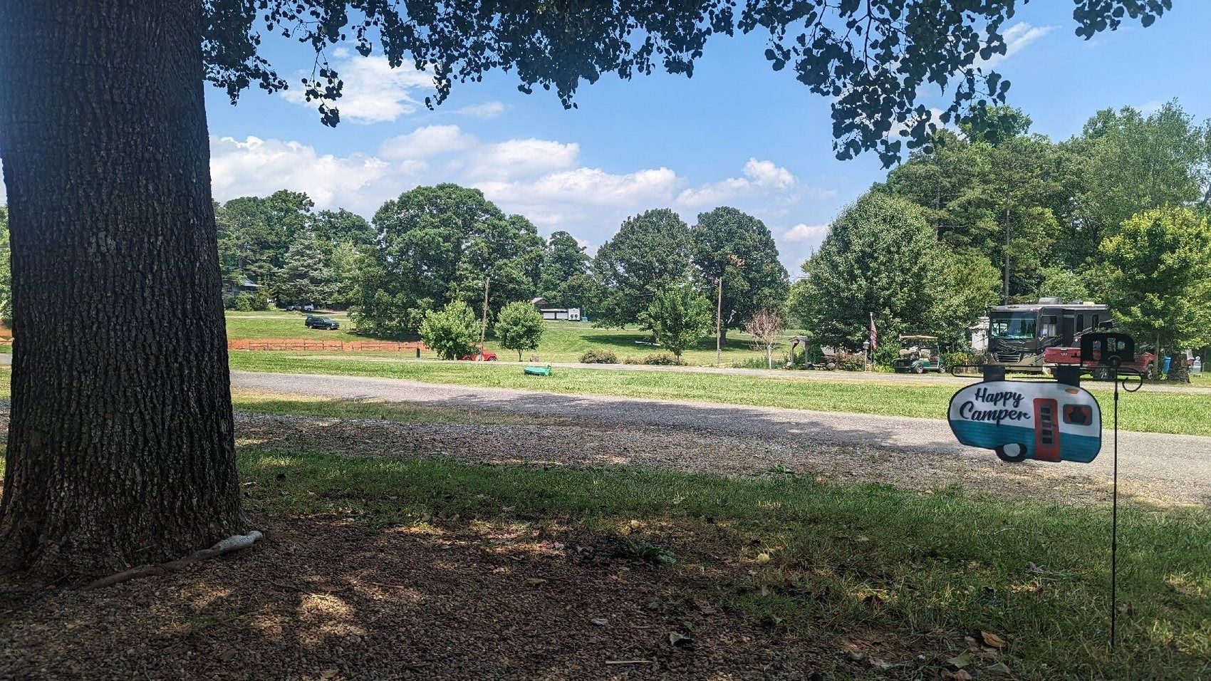 Shaded park with a gravel path, trees, and a small blue lawnmower or cart in the distance