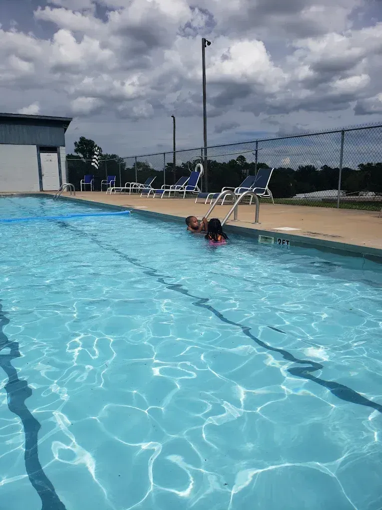 Person at the edge of a public swimming pool under a cloudy sky