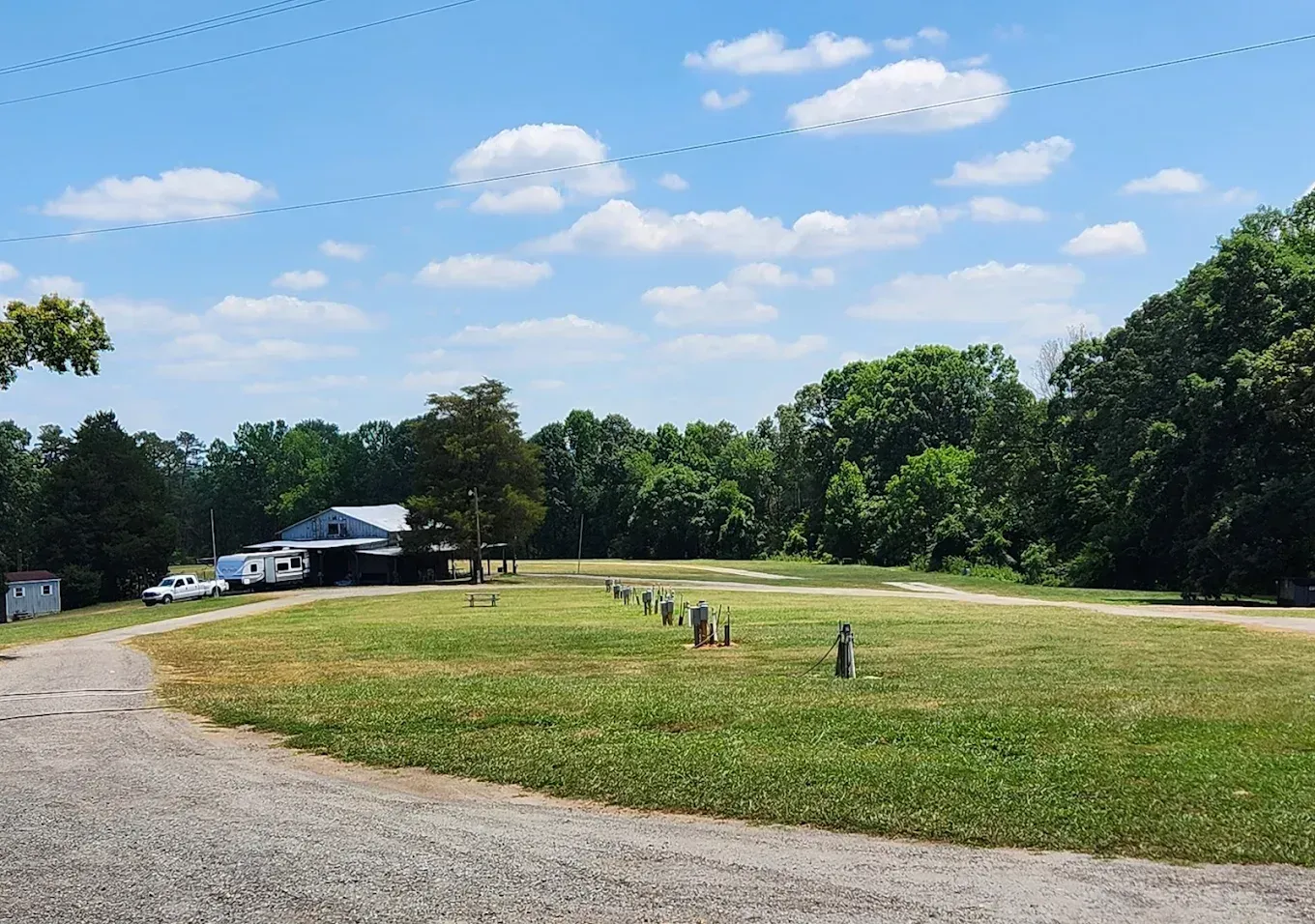 Gravel path beside a grassy field with people and parked vehicles under a blue sky with clouds