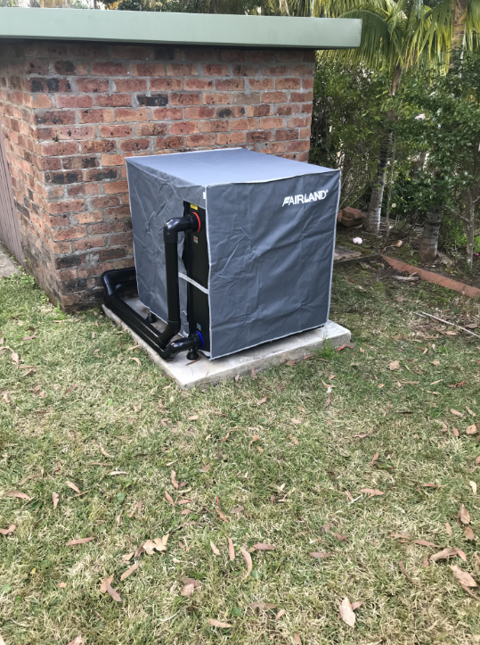 A Machine is Sitting in the Grass in Front of a Brick Building — Newcastle Solar Pool Heating Systems In Singleton, NSW