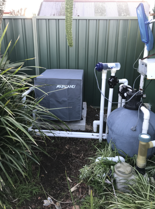 A Pool Pump is Sitting in the Grass Next to a Fence — Newcastle Solar Pool Heating Systems In Gosford, NSW