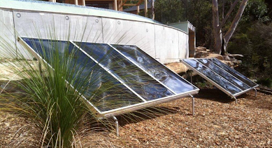 Three Solar Panels Are Sitting in the Dirt in Front of a Greenhouse — Newcastle Solar Pool Heating Systems In Wyong, NSW