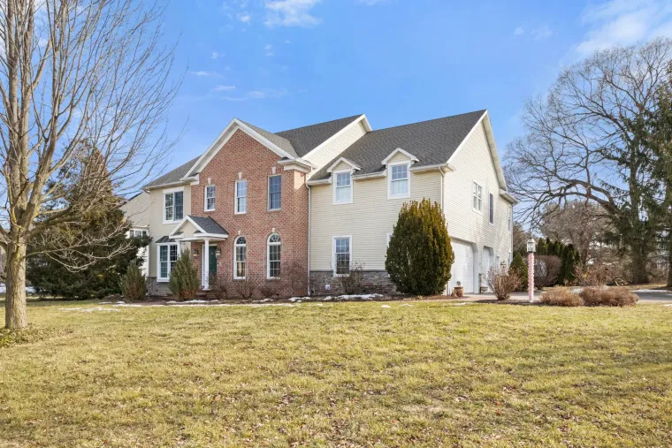 Large two-story brick and white house with a wide front lawn and leafless trees on a sunny day