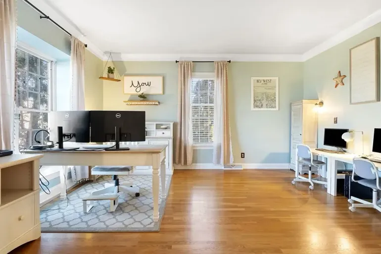 Bright home office with desks, computers, hardwood floors, and large windows filling the room with light