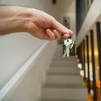 Hand holding keys in a hallway with stairs and warm lights in the background