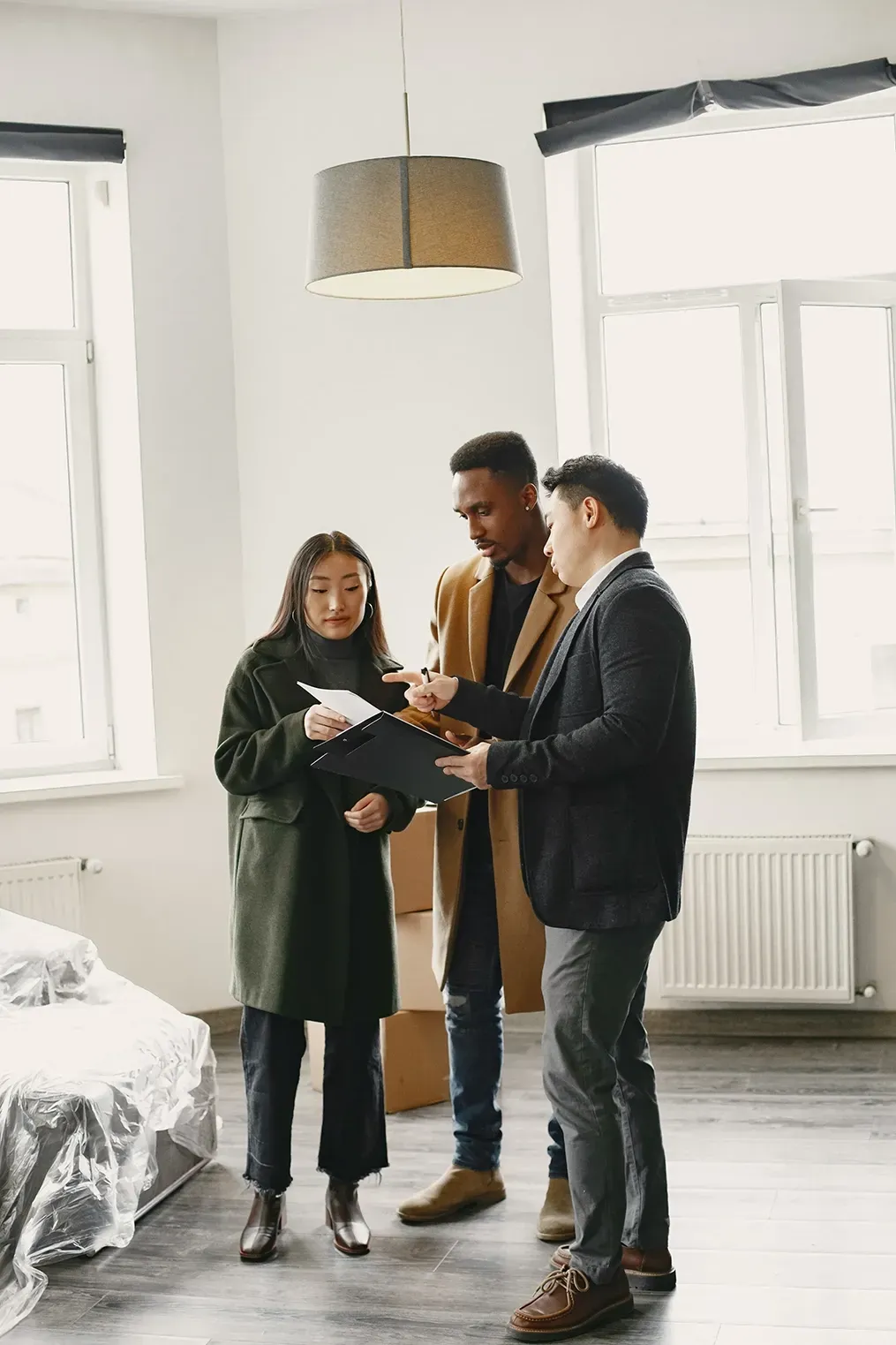 Three people discussing a document in a bright, empty room with large windows