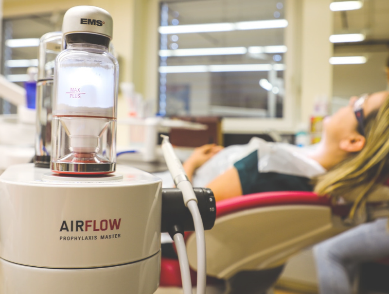 A woman is sitting in a dental chair next to an airflow machine